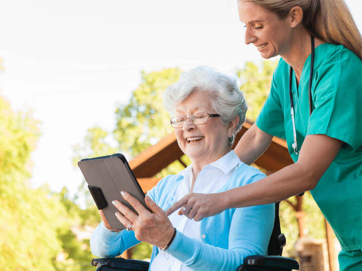 Ältere Frau im Rollstuhl, die von einem Ärztepersonal eine Erklärung auf dem Tablet bekommt